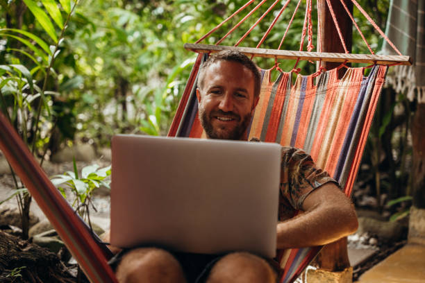 istock Man Relaxing in Hammock with Laptop in Tropical Setting 2195171886