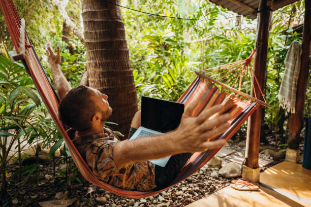 istock Man Relaxing in Hammock with Laptop in Tropical Garden 2195172525