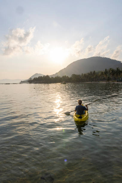 istock Man paddles kayak towards mountains at sunrise 2195173018