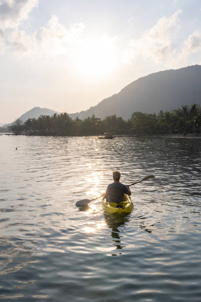 istock Man paddles kayak towards mountains at sunrise 2195173119