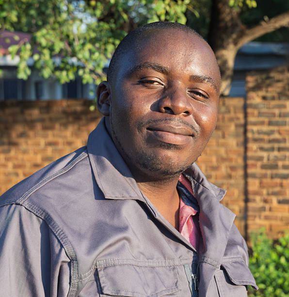 istock Smiling single African overweight man in workwear , outdoors with a brick wall background, standing, expressing happiness, bright natural sunlight, casual pose, South Africa, daytime 2195173342