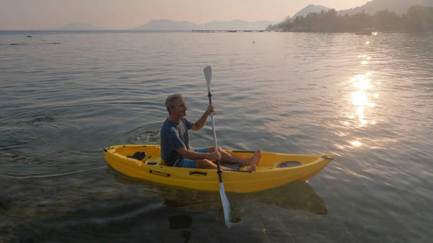 istock Man paddles kayak towards mountains at sunrise 2195173538