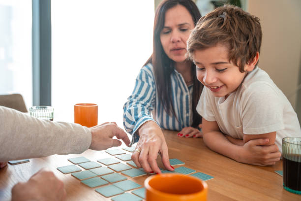 A smiling Hispanic family, including a mother and young son, engages in a cheerful puzzle activity on a dining table. Natural light brightens the warm, homely atmosphere as they enjoy a leisurely afternoon.