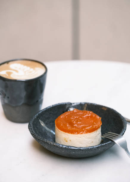 istock Delicate mini cheesecake with glossy apricot glaze, served on an artisan ceramic plate alongside a creamy cappuccino, elegant dessert presentation, fine patisserie sweet treat, bakery branding and café menu concept 2195180407