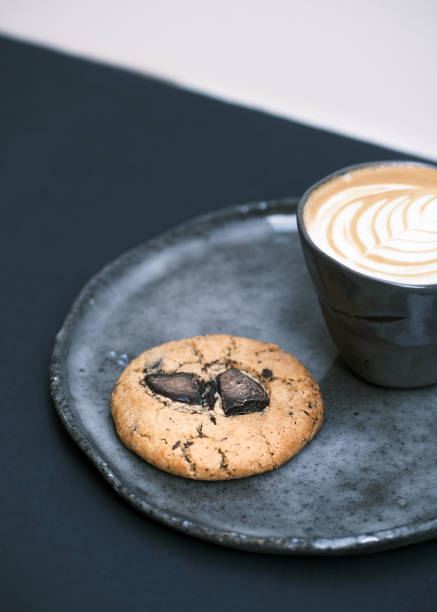 Gourmet chocolate chip cookie with a cracked surface served on a rustic ceramic plate, accompanied by a cup of latte with beautiful latte art, cozy café ambiance, artisanal bakery concept, perfect for food photography and branding
