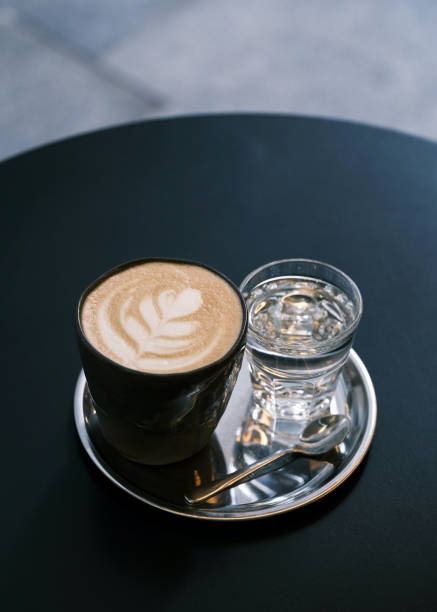 istock Elegant coffee presentation with latte art in a glass cup on a silver tray, accompanied by a glass of water and spoon, modern café ambiance, specialty coffee culture, barista craftsmanship, minimalist coffee setup 2195180545