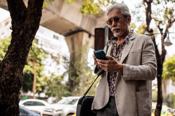 istock Senior Thai Man Using Mobile Phone in Downtown Bangkok 2195194223