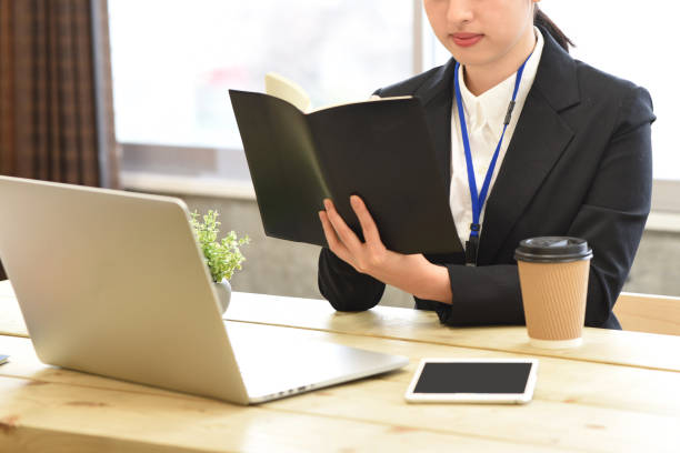 A young woman in a suit checking notes in front of a laptop computer