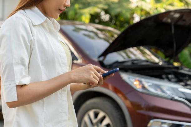 istock breakdown, broken car, repair. Woman uses mobile phone check insurance premiums through application due to car accident . Find garage to get car fixed during country tour, waiting for help, emergency. 2195201943