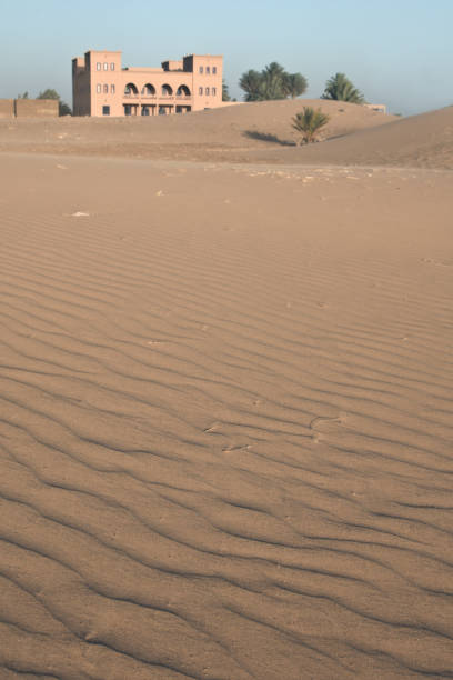 Sahara Desert; Morocco - June 23, 2010: Pink Kasbah stands in rippled sand dunes.