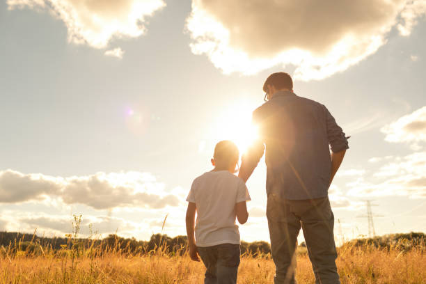 padre e figlio che si legano nella natura, in piedi nel prato a guardare il tramonto, trascorrendo del tempo di qualità insieme. - festa del papà foto e immagini stock