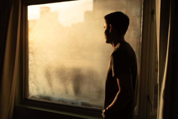istock Thoughtful man in city apartment looking out his window. 2195204759