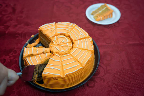 Hand using a spatula to serve a slice of orange halloween spiderweb cake