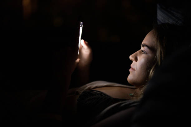 Profile view of young woman reading a text message on smart phone in the dark. Copy space.