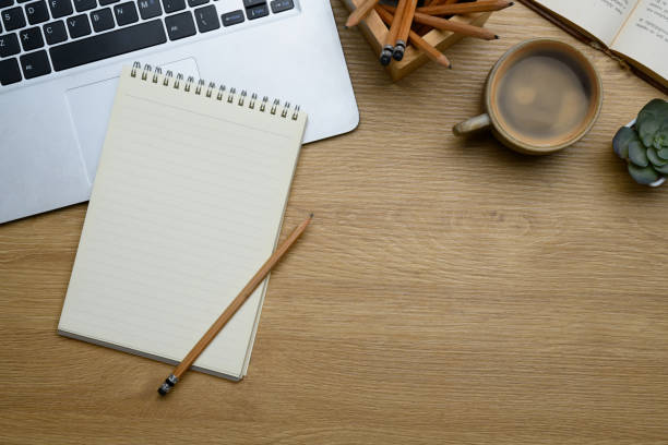 istock Empty spiral notepad, a cup of coffee, and laptop on wooden desk surface 2195212145