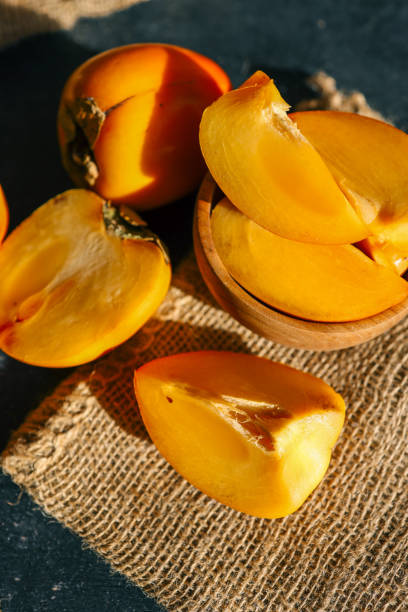 istock Sliced and whole persimmons arranged on a dark textured surface with natural light and burlap, showcasing vibrant colors and rustic simplicity. Perfect for food, seasonal, and healthy living themes 2195212214