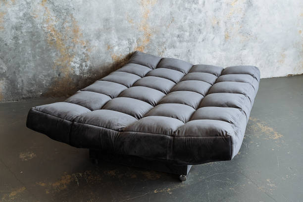 istock A grey futon is currently positioned on a bare concrete floor, which is directly in front of a cold, solid concrete wall, creating a unique and minimalist aesthetic in the room 2195217845