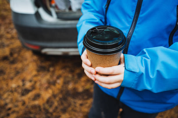 istock An individual stands gracefully, dressed in a chic blue jacket, cradling a steaming coffee cup in hand, while a car parks behind, enhancing the richness of this captivating scene 2195218774