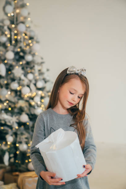 istock Cute little girl with gift in box and christmas tree 2195225468