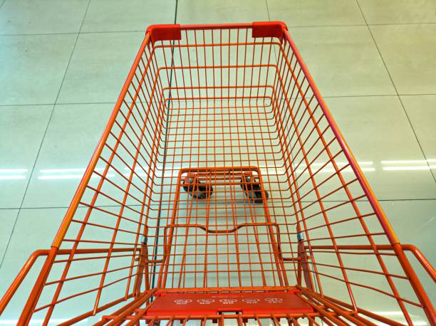 An empty orange shopping cart with a wireframe design is seen from above on a tiled floor. The cart is positioned in a well-lit, clean environment, likely a supermarket or store