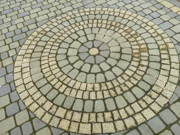 istock Circular pattern on a sidewalk made of yellow and gray paving stones. Decorative pattern made of paving stones. 2195227312