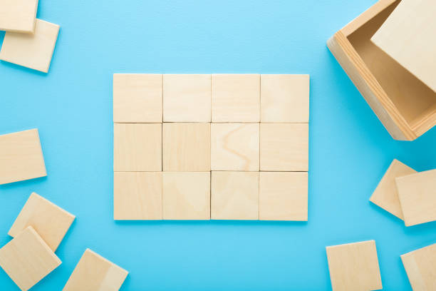 istock Wooden puzzle square pieces with box on light blue table background. Pastel color. Closeup. Finished jigsaw. Children development game. Top down view. 2195229002