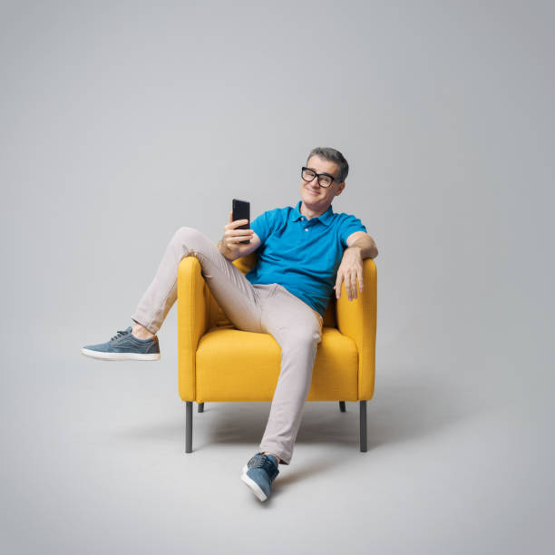 istock Happy man relaxing on an armchair and using his phone 2195230340