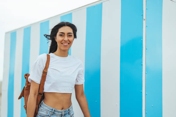 istock Smiling Woman Walking Outdoors With Backpack by Blue and White Striped Wall 2195230344
