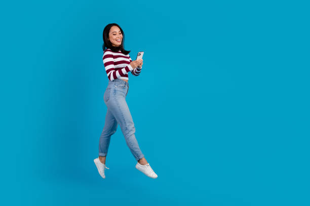istock Young woman in casual outfit smiling while browsing on smartphone over blue background 2195231500