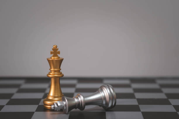 istock Gold chess king stands tall with silver king lying on its side, symbolizing victory and defeat on a checkered board. 2195232771