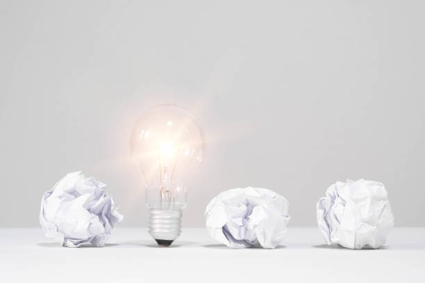 Illuminated light bulb among crumpled paper balls, symbolizing innovation and creative ideas amidst failures.