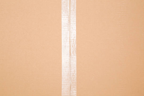 Transparent scotch tape on closed brown carton pack. Closeup. Top down view.