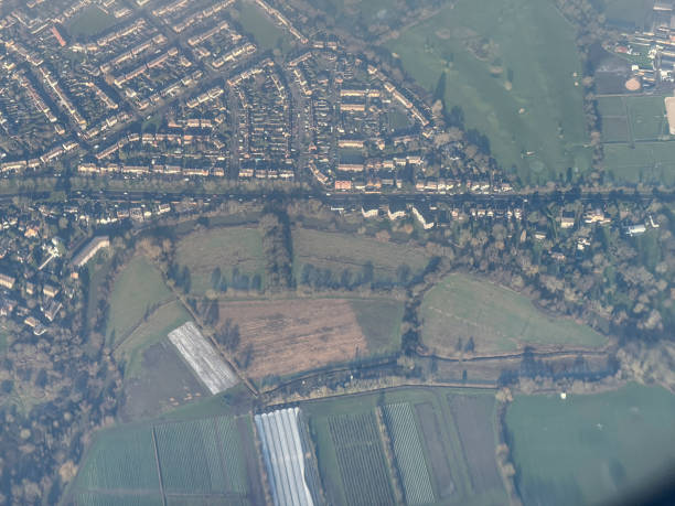 Aerial view of an ancient stone pathway winding through vibrant green fields, suggesting historical significance and natural beauty. The path's linear structure contrasts with the organic shapes of the surrounding vegetation, creating a sense of timelessness and exploration.