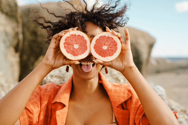 Smiling Woman Playfully Posing Outdoors with Grapefruit Halves in Nature