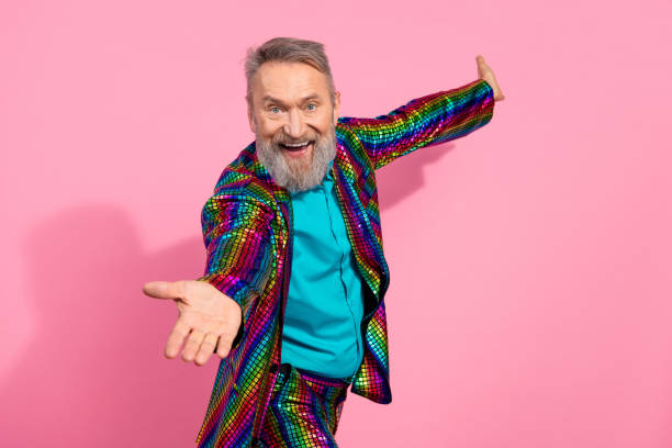 istock Elderly Man in Vibrant Multicolored Suit on Pink Background Poses Cheerfully Representing Fun, Glamour, and Energetic Style 2195235263