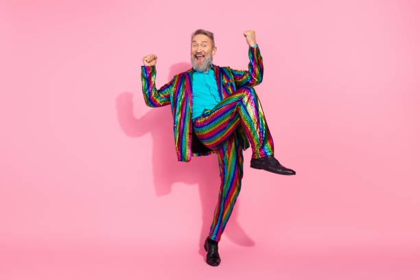 istock Charismatic elderly man celebrating in a rainbow-striped suit, posing dynamically against a vibrant pink background 2195235278