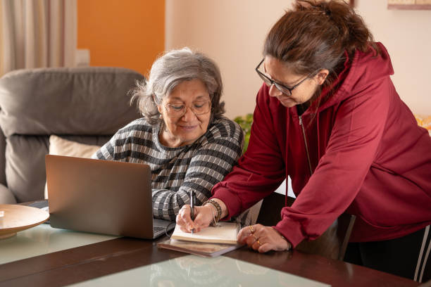istock Middle-aged woman jotting on a notepad while her elderly mother watches on the computer 2195235367