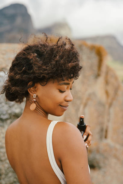 istock Young Woman Spraying Sunscreen On Her Skin Outdoors with a Serene Mountain Backdrop 2195235563