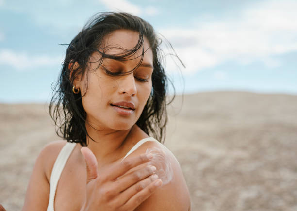 Young Woman Applying Sunscreen Under a Clear Blue Sky in a Sunny Outdoor Setting