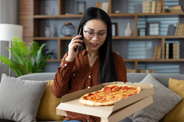istock Young woman enjoying pizza delivery at home while chatting on smartphone, feeling relaxed and happy in cozy living room setting, appreciating delicious comfort food and modern communication. 2195236104