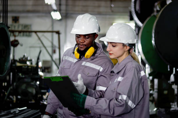 istock Harmony diversity people working together. Industrial engineer woman discussing with her African coworker. Workers with protective workwear and helmet work at manufacturing factory metal industry. 2195236259