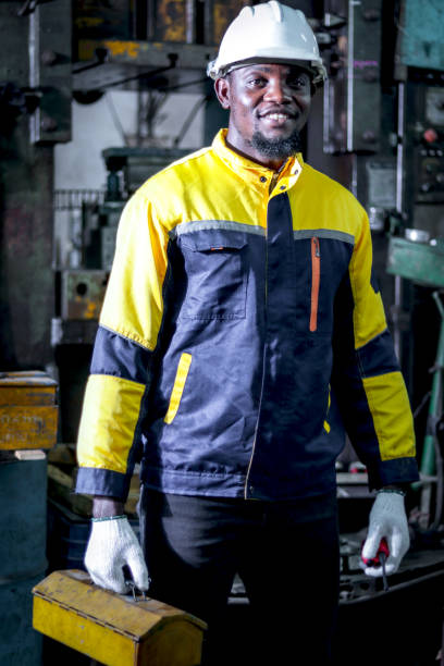 istock African industrial engineer man with protective workwear and safely helmet holding toolbox while inspecting machine at manufacturing factory. Happy worker repairing machinery at steelmaking industry. 2195236414