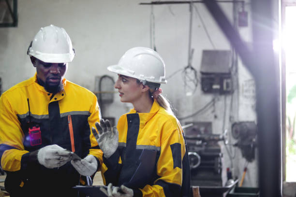 istock Harmony diversity people working together. Industrial engineer woman discussing with her African coworker. Workers with protective workwear and helmet work at manufacturing factory metal industry. 2195236419