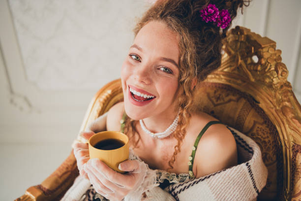 An attractive lady dressed in glamorous vintage attire, smiling while holding a cup of coffee, exuding an air of elegance, charm, and nostalgia in an ornate and luxurious interior setting.