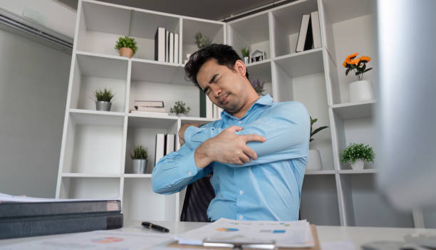 istock Young Businessman in Modern Office Experiencing Aches and Pains While Working at Desk with Documents and Laptop 2195241394