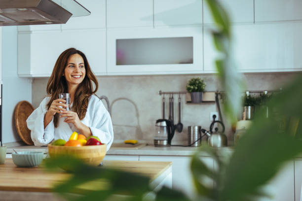 Woman Drinking Water in Modern Kitchen With Fresh Fruit Bowl