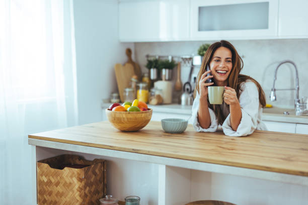 istock Woman Talking On Phone And Enjoying Coffee In Bright Kitchen 2195248469