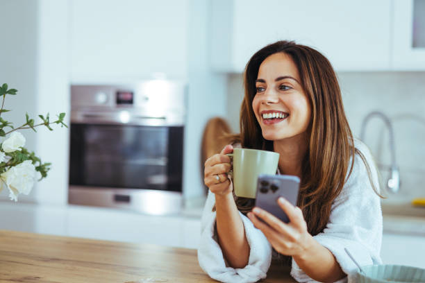 istock Smiling Woman Enjoying Coffee and Checking Her Smartphone in Kitchen 2195248472