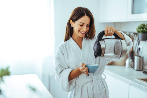 istock Smiling Woman in Bathrobe Pouring Coffee in Modern Kitchen Setting 2195248486