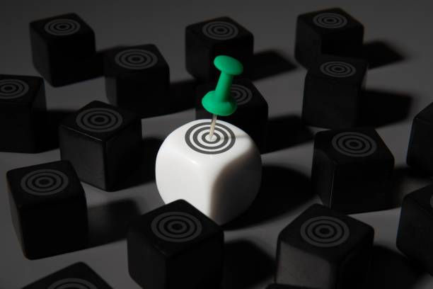 A white cube with a target and a green pushpin stands out among a black cubes. Goal setting, target setting, focus concept.